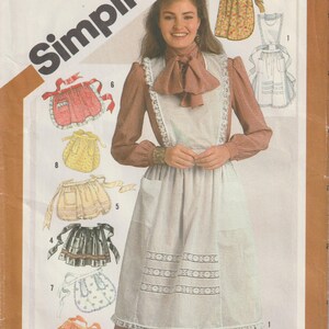 May include: A sewing pattern for a white apron with lace trim and a brown blouse. The pattern includes eight different apron designs, including a red and white gingham apron, a yellow polka dot apron, and a floral print apron. The pattern is for size one and costs $2.50. Simplicity 5323.