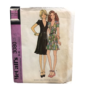 May include: Vintage McCall's 3080 sewing pattern for Misses' and Junior Petite dresses. The pattern envelope features illustrations of two dresses: a black wrap dress and a colorful floral print dress. The envelope includes the text "STEP-BY-STEP PATTERN".