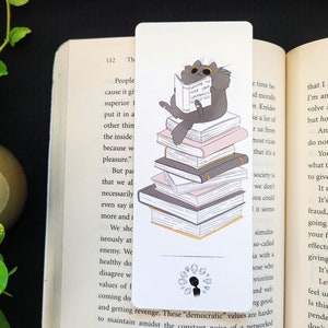 May include: A black cat wearing sunglasses sits on a stack of books and reads a book titled "Ways to Kick Your Cat's Butt". The cat is surrounded by a ring of small black and white diamonds.