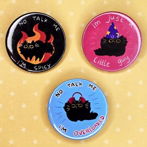 May include: Three round black and white buttons with black cat illustrations. The first button says "No Talk Me I'm Spicy" with a cat in flames. The second button says "Im Just A Little Guy" with a cat wearing a wizard hat. The third button says "No Talk Me I'm Overloaded" with a cat wearing headphones.