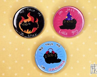 May include: Three round black and white buttons with black cat illustrations. The first button says "No Talk Me I'm Spicy" with a cat in flames. The second button says "Im Just A Little Guy" with a cat wearing a wizard hat. The third button says "No Talk Me I'm Overloaded" with a cat wearing headphones.