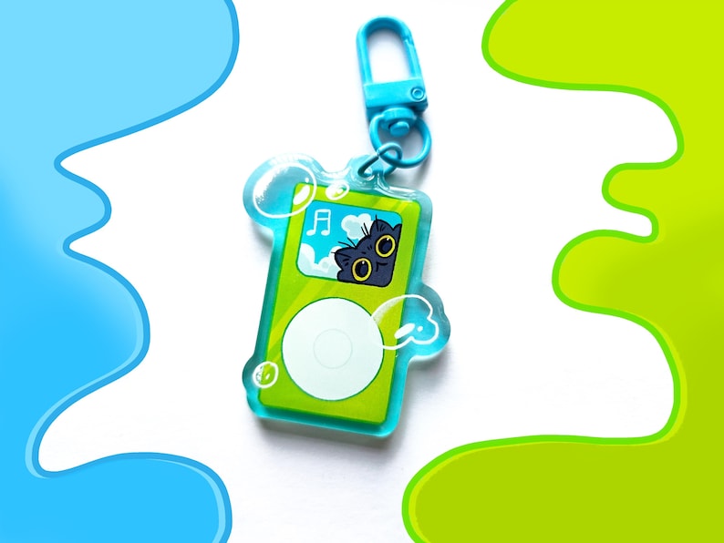 May include: A green and white keychain shaped like a music player, featuring a cartoon cat with yellow eyes. The keychain has a blue clasp and is surrounded by bubble-like shapes. The background has blue and green abstract designs.