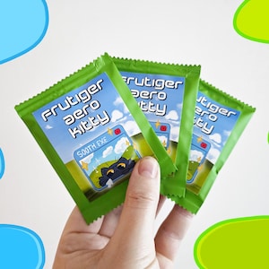 May include: Three green packets are held in a hand. Each packet has the text "Frutiger Aero Kitty" in blue and white, with a cartoon cat graphic. The packets are against a white background with blue and green shapes.