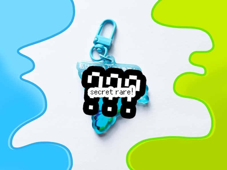 May include: A light blue keychain with a matching clasp. The keychain has a clear, iridescent charm with a black and white pixelated design that reads "secret rare!". The background has blue and green paint splotches.