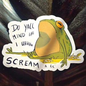 May include: A white sticker with a cartoon frog on it. The frog is green with yellow spots and has its mouth open. The text on the sticker says "Do yall mind if I uhhh scream a lil'"