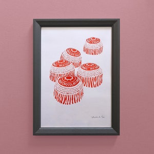 May include: A framed print of five red and white milk chocolate malt balls. The print is on white paper with a black frame.