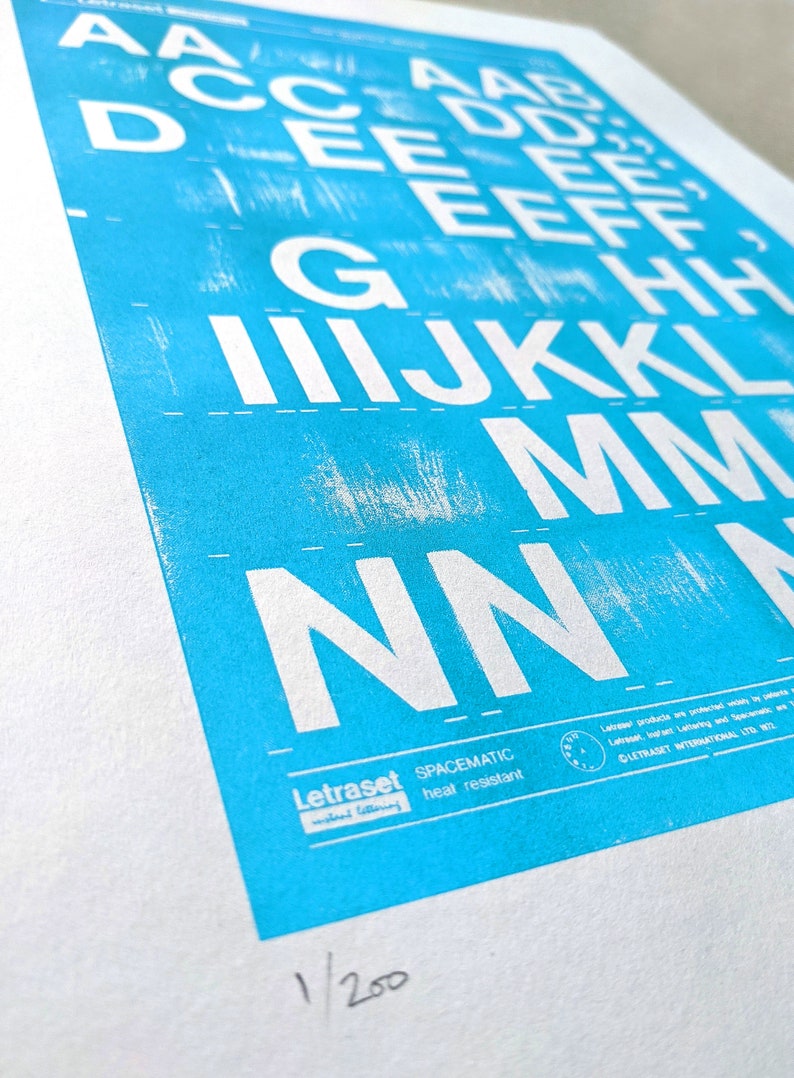 May include: A blue and white print of the alphabet, with the letters A through N, printed in white on a blue background. The print is numbered 1/200 and includes the text "Letraset SPACEMATIC heat resistant".