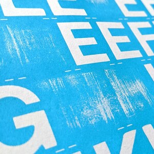 May include: A close-up of a blue background with white letters printed on it. The letters are in a repeating pattern and include the letters E and G.