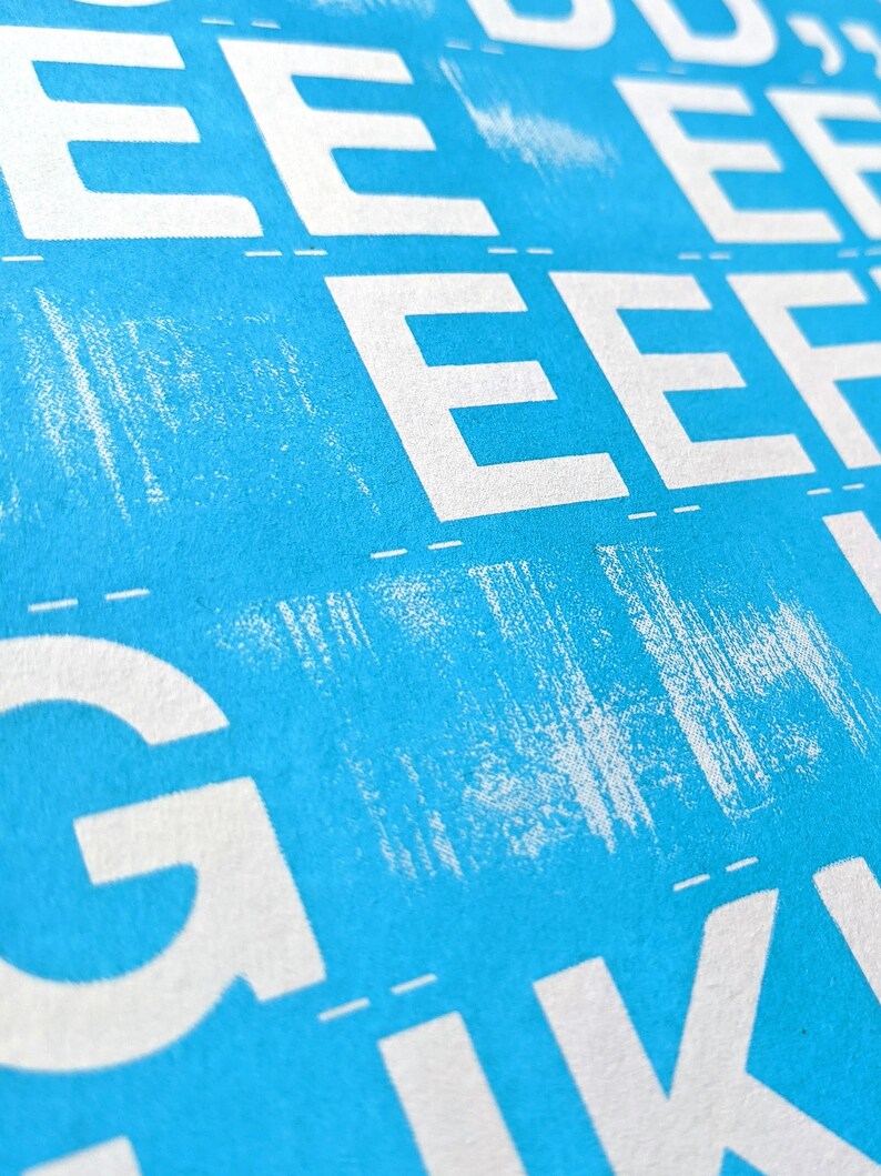 May include: A close-up of a blue background with white letters printed on it. The letters are in a repeating pattern and include the letters E and G.