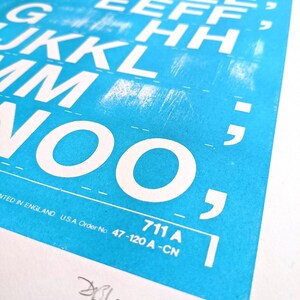 May include: A close-up of a blue poster with white letters printed in a blocky font. The letters are arranged in columns, starting with the letter "A" and ending with the letter "O". The poster also includes the text "711 A" and "NTED IN ENGLAND U.S.A. Order No 47-120 A-CN".