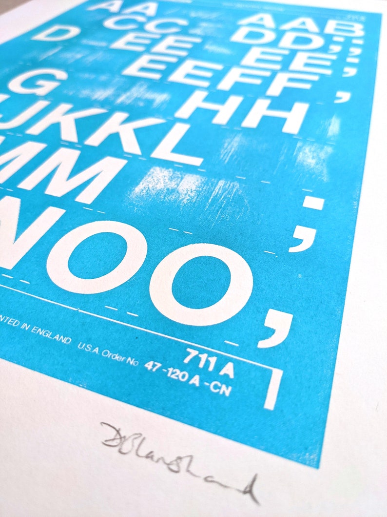 May include: A close-up of a blue poster with white letters printed in a blocky font. The letters are arranged in columns, starting with the letter "A" and ending with the letter "O". The poster also includes the text "711 A" and "NTED IN ENGLAND U.S.A. Order No 47-120 A-CN".