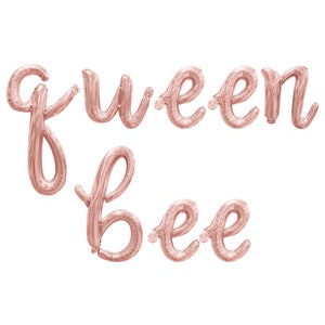 May include: Rose gold foil balloons spelling out the words "queen bee" in a cursive font. The balloons are inflated and ready for a party or celebration. The letters are connected and have a shiny metallic finish.