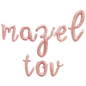 May include: Rose gold foil balloon letters spelling out "mazel tov" in a cursive font. The balloons are inflated and arranged against a white background, suitable for a celebration.