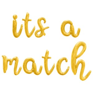 May include: Gold foil balloon letters spelling out "its a match" on a white background. The letters are in a cursive font, perfect for a wedding or engagement announcement.