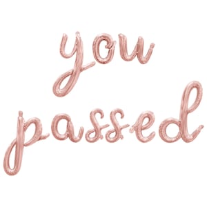 May include: Rose gold foil balloons spelling out the words "you passed" in a cursive font. The balloons are inflated and arranged against a white background, perfect for a graduation or celebratory event.