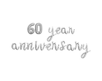 May include: Silver foil balloon letters spelling out "60 year anniversary" on a white background. The number "60" is in a bold font, while the words "year anniversary" are in a cursive font. Ideal for milestone celebrations.