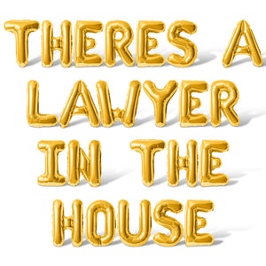 May include: Gold foil balloons spelling out the phrase "There's a lawyer in the house".