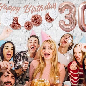 May include: A group of friends celebrating a 30th birthday with rose gold balloons, confetti, and sparklers. The banner reads "Happy Birthday".
