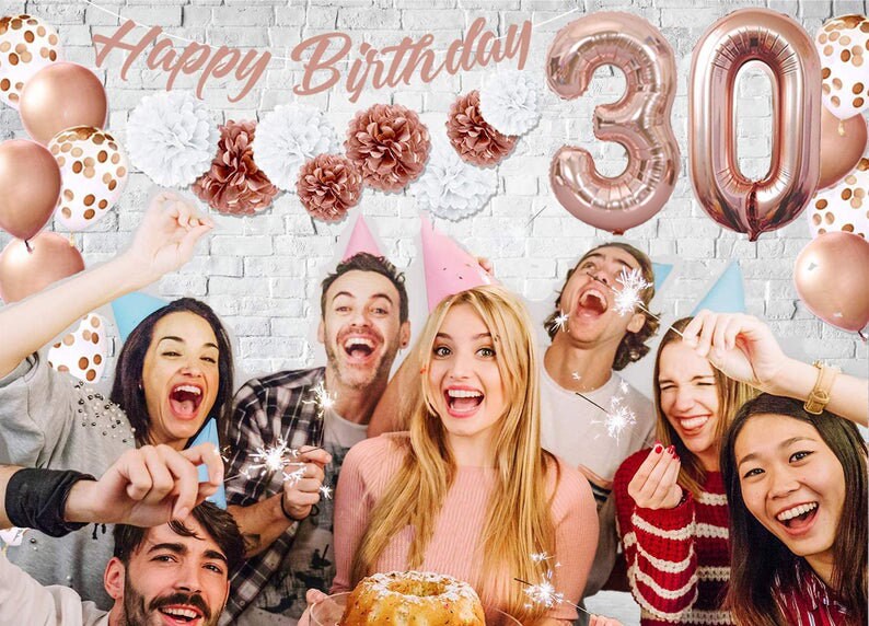May include: A group of friends celebrating a 30th birthday with rose gold balloons, confetti, and sparklers. The banner reads "Happy Birthday".