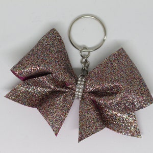 May include: A sparkly multi-coloured glitter bow with a silver rhinestone accent attached to a silver key chain.