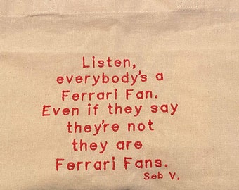 Könnte beinhalten: Eine beige Canvas-Tragetasche mit rotem Sticktext, der "Listen, everybody's a Ferrari Fan. Even if they say they're not they are Ferrari Fans. Seb V." lautet.