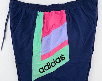 May include: Navy blue athletic shorts with a colorful panel featuring pink, light purple, and mint green sections. The Adidas logo is printed in black. The shorts have an elastic waistband and a drawstring.