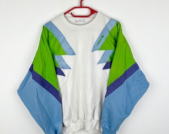 May include: White sweatshirt with green, blue, and purple geometric patterns. The sweatshirt has the Adidas logo in green on the front.
