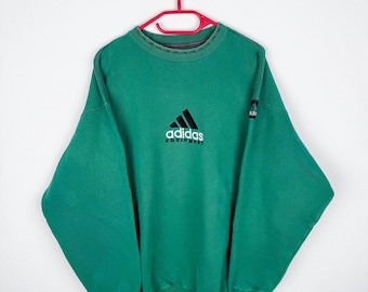 May include: Green Adidas Equipment sweatshirt with a black and white logo on the front. The sweatshirt has a crew neck and long sleeves.