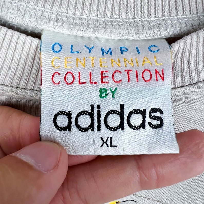 May include: White Adidas sweatshirt with a tag that reads "Olympic Centennial Collection by Adidas" in colorful lettering. The tag also says "XL".