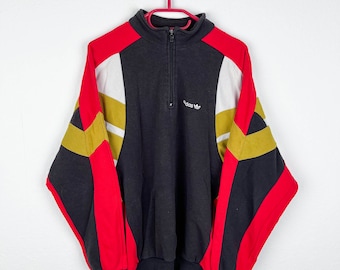 May include: A vintage Adidas sweatshirt in black, red, white and gold with a half-zip closure and the Adidas logo on the front.