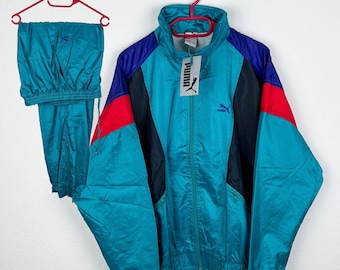 May include: A vintage Puma track suit in teal, blue, red, and black. The jacket has a zip-up front, a high collar, and the Puma logo. Matching track pants are also included. The set is displayed on a red hanger against a white background.