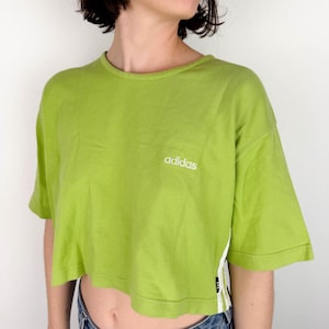 May include: A lime green cropped t-shirt with short sleeves and a white "adidas" logo on the front.