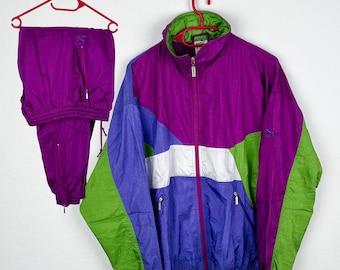 Puede incluir: Un chándal morado, verde, blanco y azul con una chaqueta con cremallera y pantalones a juego. La chaqueta tiene un diseño de bloques de color con una franja blanca en el pecho.