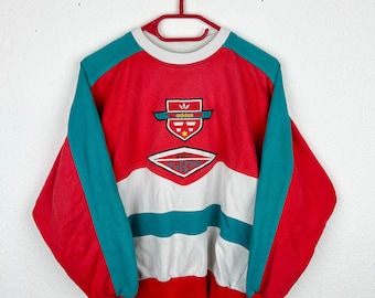 May include: Red, white, and teal vintage Adidas sweatshirt with a large embroidered logo that says "adidas" and "Sports Collection".