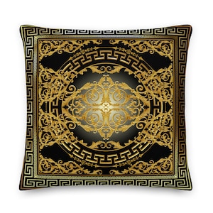 Op de afbeelding: Een zwart en gouden decoratief kussen met een Griekse sleutelrand en een ingewikkeld bloemmotief in het midden.
