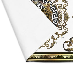 May include: A white background with a gold and black ornate design. The design features a circular pattern with a Greek key border and intricate floral details.