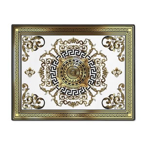 May include: A white square rug with a gold and black geometric design. The design features a central circle with a smaller circle inside, surrounded by a Greek key pattern. The rug has a black border.