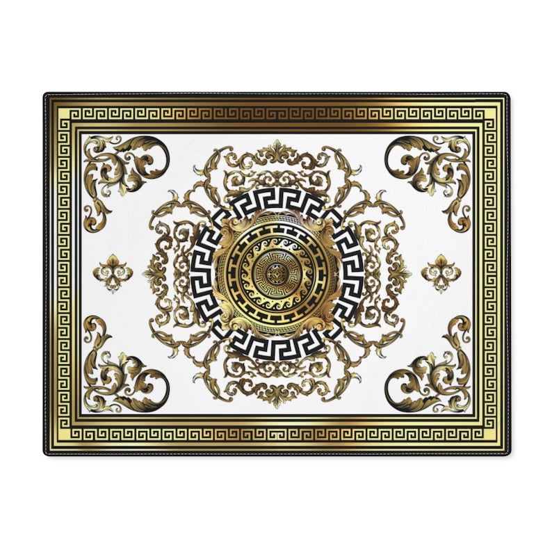 May include: A white square rug with a gold and black geometric design. The design features a central circle with a smaller circle inside, surrounded by a Greek key pattern. The rug has a black border.