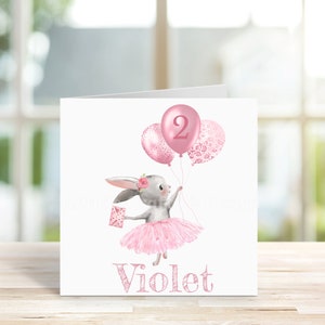 May include: A pink and gray bunny wearing a pink tutu holds a pink balloon with the number 2 on it. The bunny is holding a small gift box. The card says "Violet" at the bottom.
