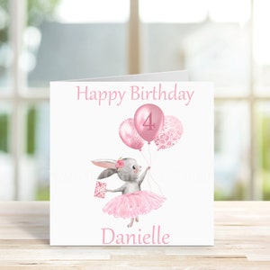 May include: A pink and white birthday card featuring a grey bunny wearing a pink tutu and holding pink balloons. The balloons have a pink "4" on one and a pink floral pattern on the others. The card reads "Happy Birthday Danielle".