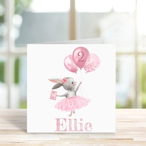 May include: A pink and white birthday card with a gray bunny wearing a pink tutu and holding pink balloons. The balloons have a pink number 2 on one and a pink floral pattern on the other. The card says "Ellie" at the bottom.