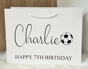 May include: White gift bag with black text and a black and white soccer ball graphic. The text reads "Charlie Happy 7th Birthday".