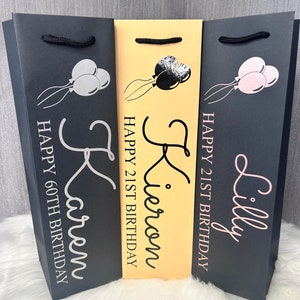 May include: Three gift bags with balloon graphics and personalized text. The bags are black and tan, with the names Karen, Kieron, and Lilly printed in silver and pink. The text includes "Happy 60th Birthday" and "Happy 21st Birthday".