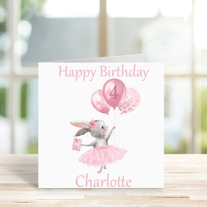 May include: A pink birthday card featuring a grey bunny wearing a pink tutu and holding pink balloons. One balloon has a pink "4" on it, while the others have a pink floral pattern. The card reads "Happy Birthday Charlotte".