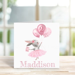 May include: A pink and white birthday card with a gray bunny wearing a pink tutu and holding pink balloons. The balloons have a pink number 2 on one and a pink floral pattern on the others. The card says "Maddison" at the bottom.