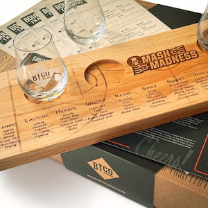 May include: A wooden tasting board with two glasses, labeled "BTCO" and "Mash Madness." The board features flavor profiles like "Tannic," "Herbal," and "Spicy." The set includes a box with care instructions.