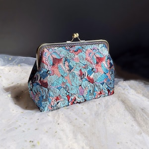 May include: A vintage-style clutch purse with a gold metal frame and a colorful floral pattern featuring butterflies. The fabric is a brocade with a blue, pink, and green color scheme.