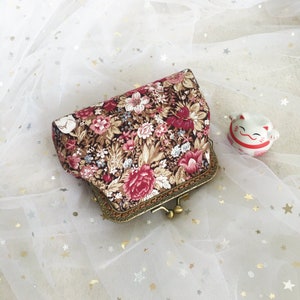 Puede incluir: Un bolso de mano de estilo vintage con estampado floral, cierre y marco de metal dorado. El bolso está sobre un fondo de tul blanco.