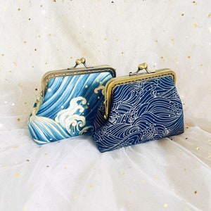 May include: Two small, clasp-top coin purses. One purse features a blue and white wave pattern, while the other has a navy blue and white wave design. Both purses have a gold-colored metal frame.