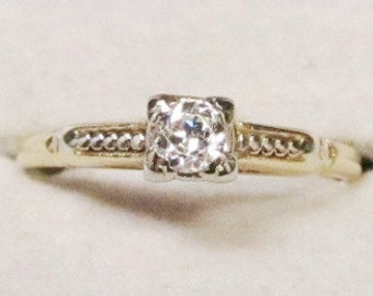 May include: A gold and silver ring with a single diamond in the center. The ring has a delicate design with a braided band.
